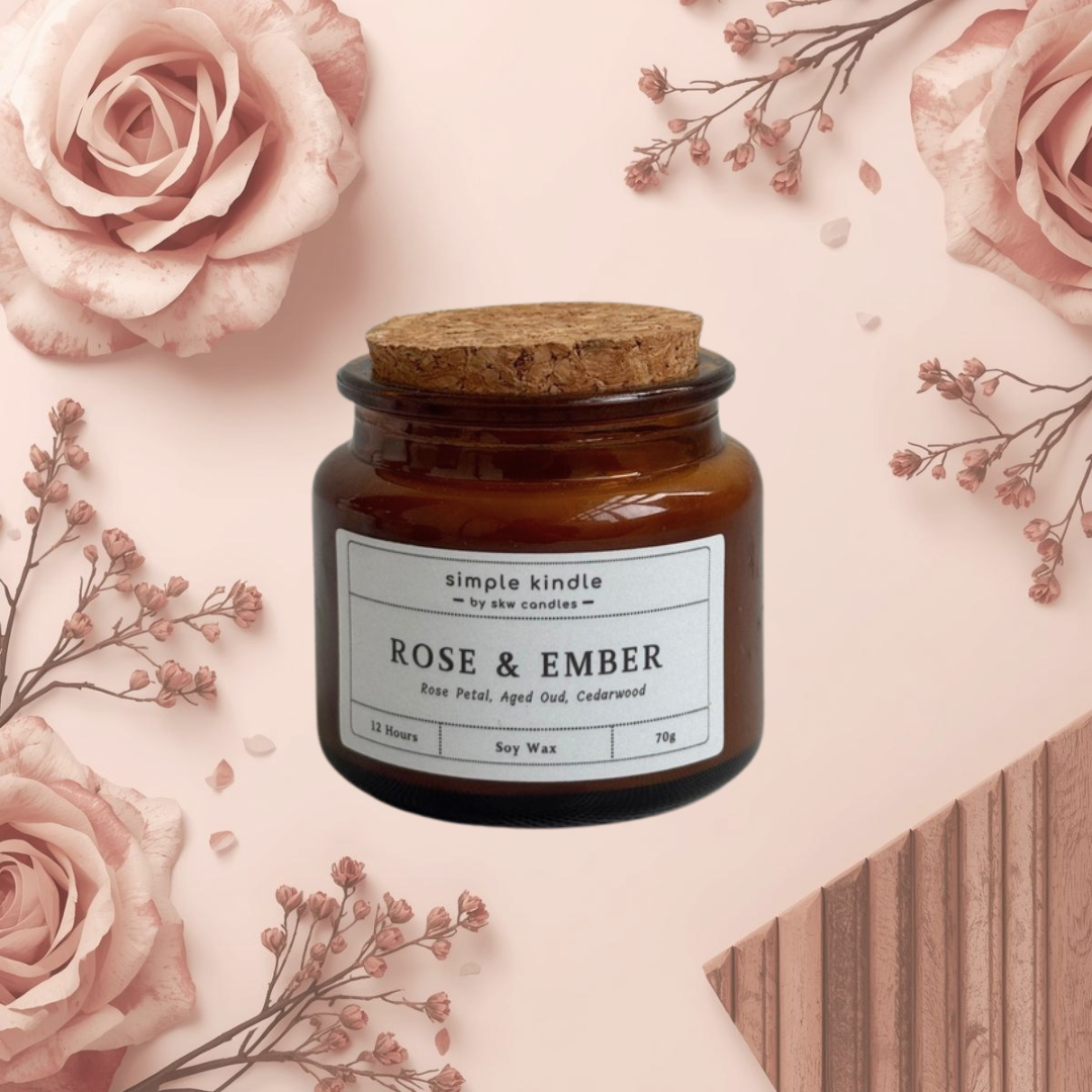 Candle jar labeled 'Rose & Ember' surrounded by pink roses and dried flowers on a light pink background