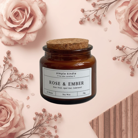 Candle jar labeled 'Rose & Ember' surrounded by pink roses and dried flowers on a light pink background